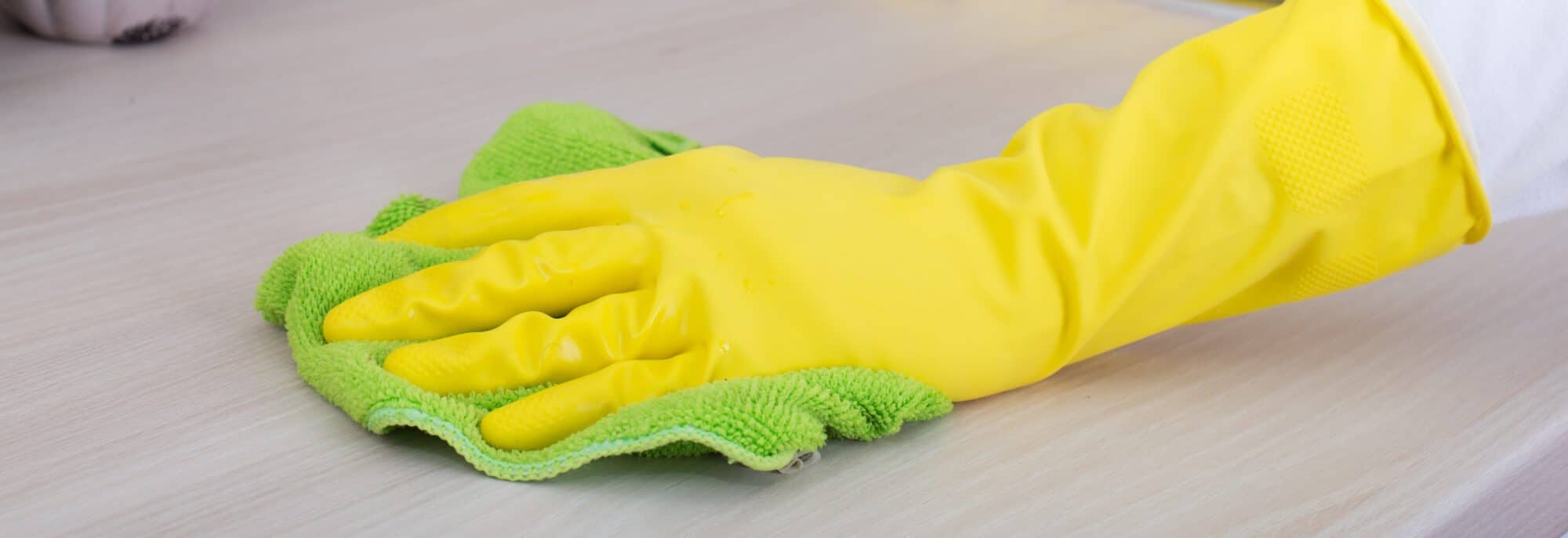 Close up of female hands with protective gloves cleaning kitchen countertop